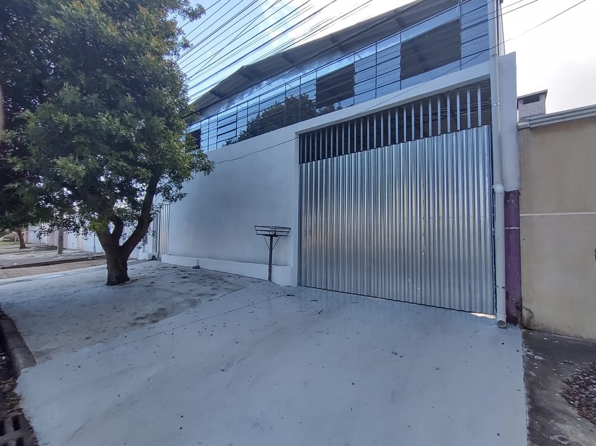 Fachada da oficina com portão metálico e árvore na calçada, em rua residencial
