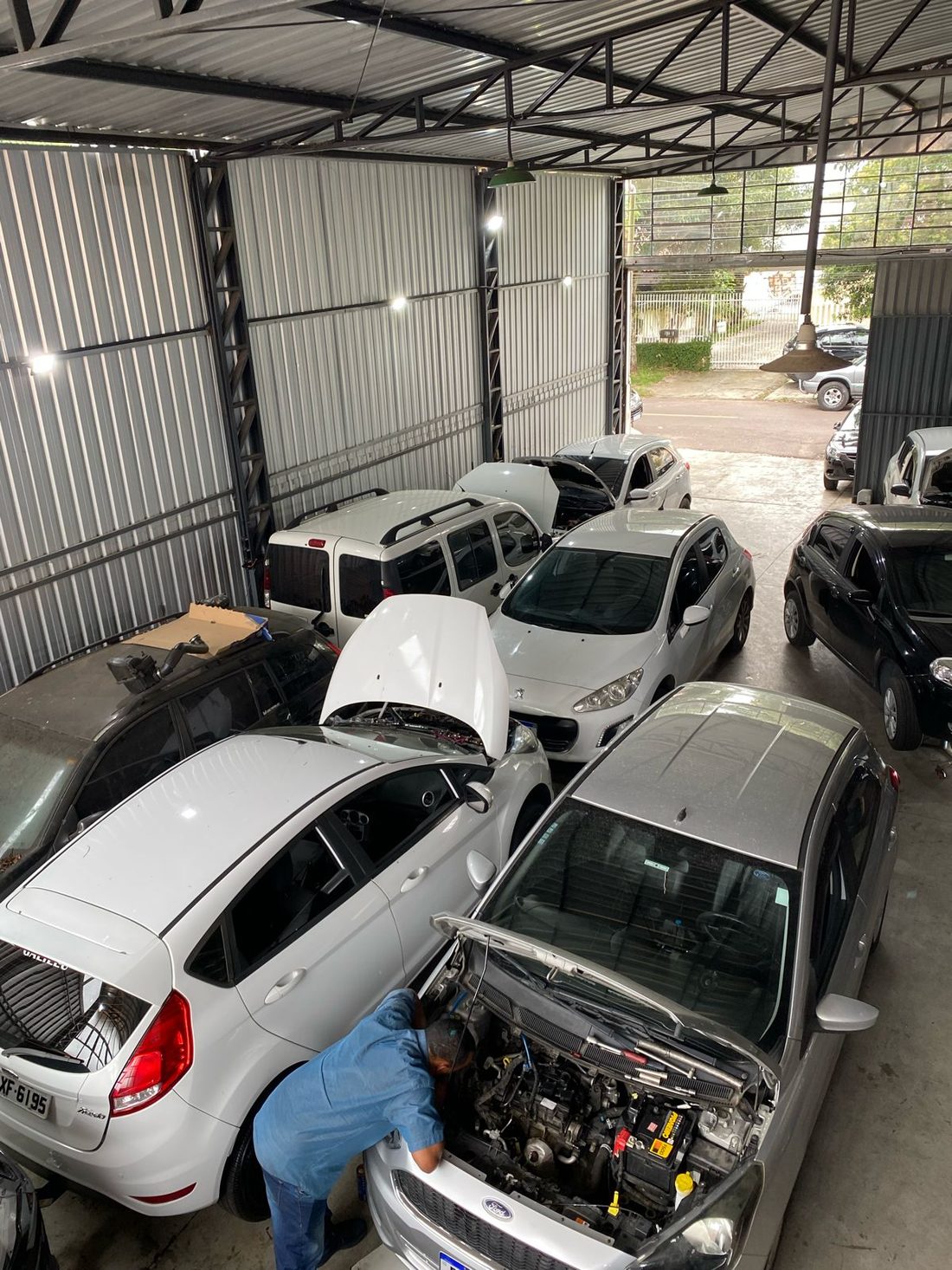 Mecânico trabalhando no compartimento do motor de um carro dentro do galpão da oficina